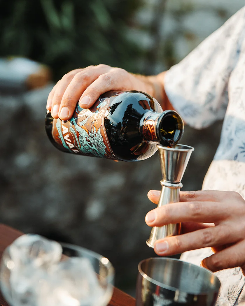 A hand pouring Laval Pelinkovac into a bar jigger during cocktail preparation.